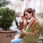 Una ragazza è seduta su una panchina con uno smartphone