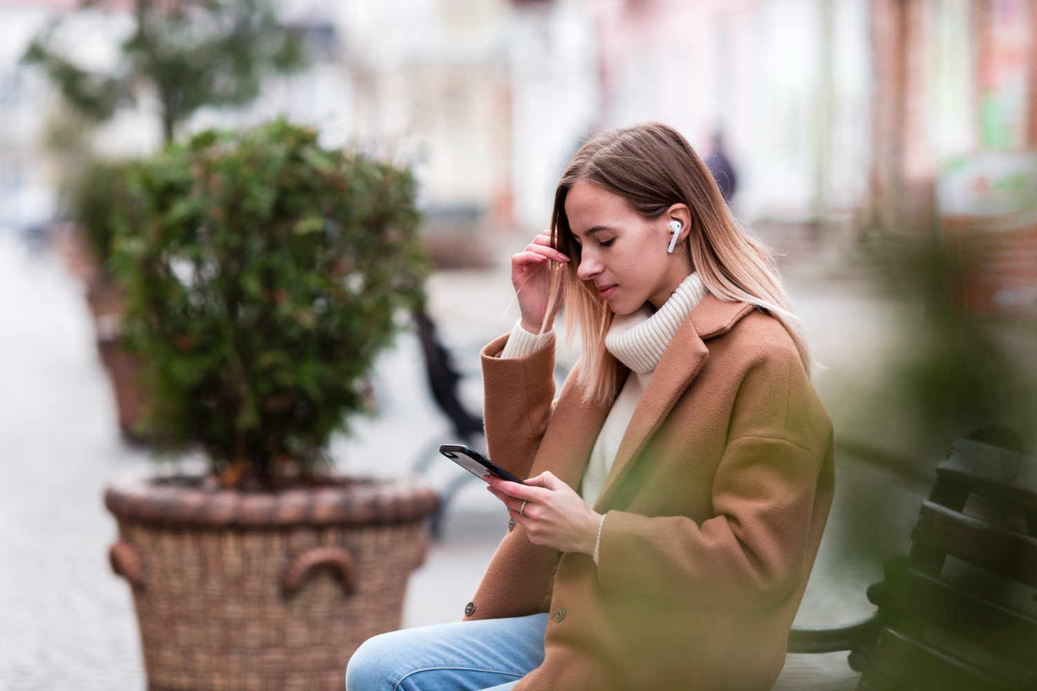 Una ragazza è seduta su una panchina con uno smartphone